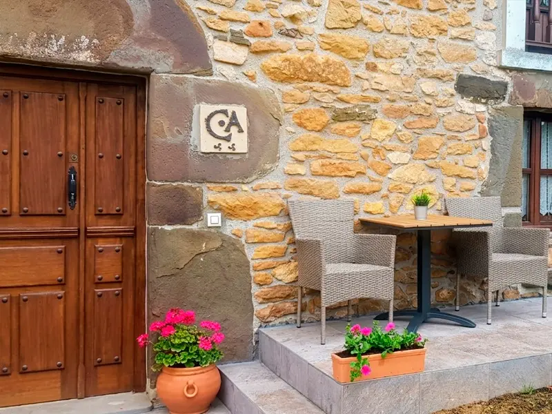 Exterior de la casa rural con la puerta de entrada y mesa con sillas.